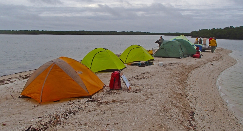 A group of tents rest on a small, sandy peninsula.